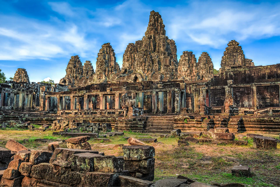 Ancient stone temple with detailed carvings, surrounded by greenery under a partly cloudy blue sky.