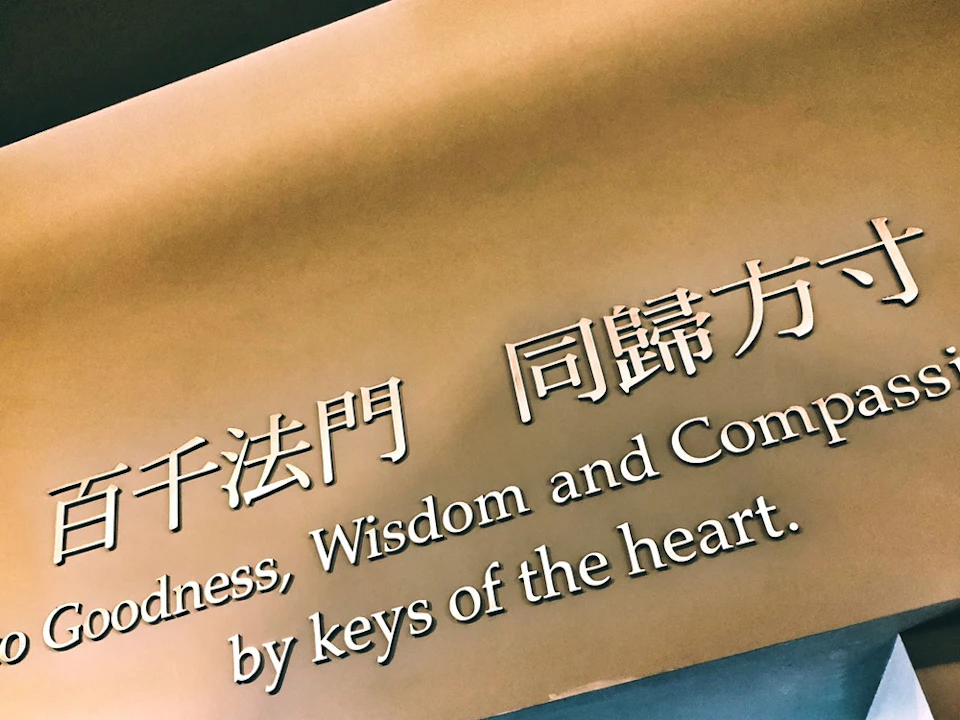 A wall with text in English and Chinese reading: "Goodness, Wisdom and Compassion by keys of the heart."