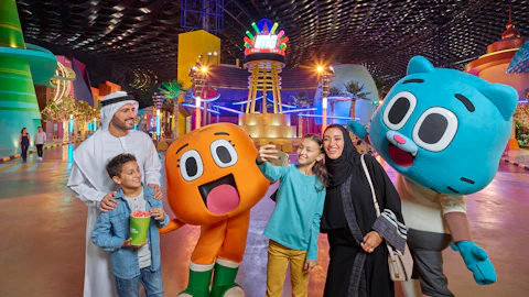 A family posing with two large cartoon character mascots inside a brightly lit indoor theme park.