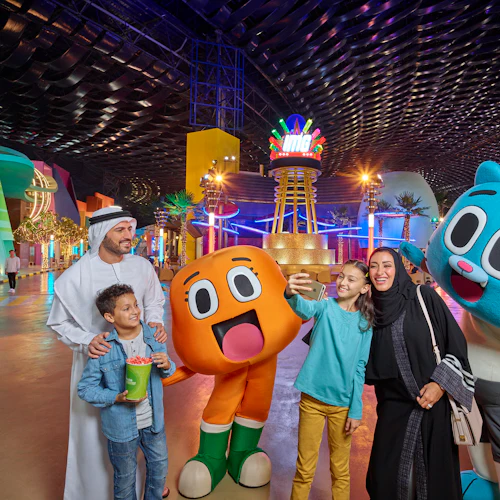 A family posing with two large cartoon character mascots inside a brightly lit indoor theme park.