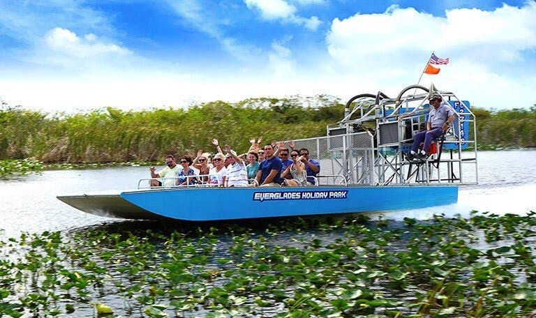 Groupe de personnes se promenant en canot pneumatique dans une zone marécageuse et verdoyante, étiquetée "Everglades Holiday Park".