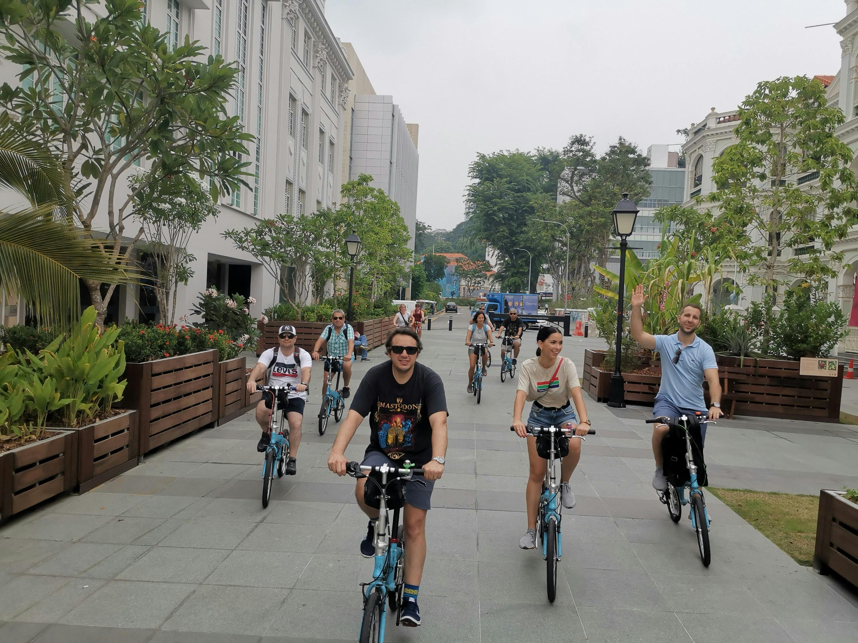 A group of people riding bicycles on a paved path in an urban area surrounded by greenery and buildings.