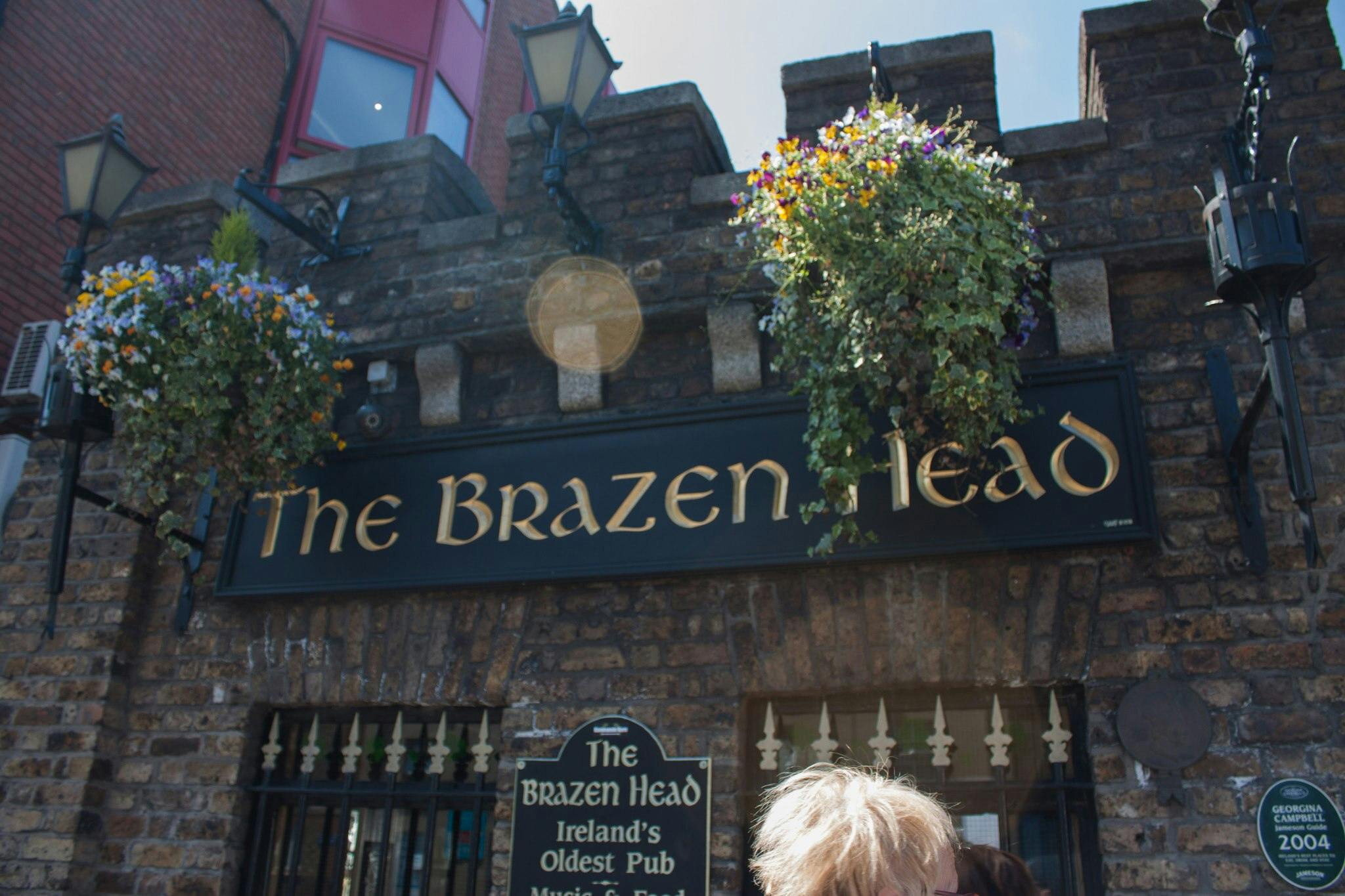 The Brazen Head pub in Dublin, with hanging flowers, lamps, and a sign stating &#34;Ireland&#39;s Oldest Pub.&#34;