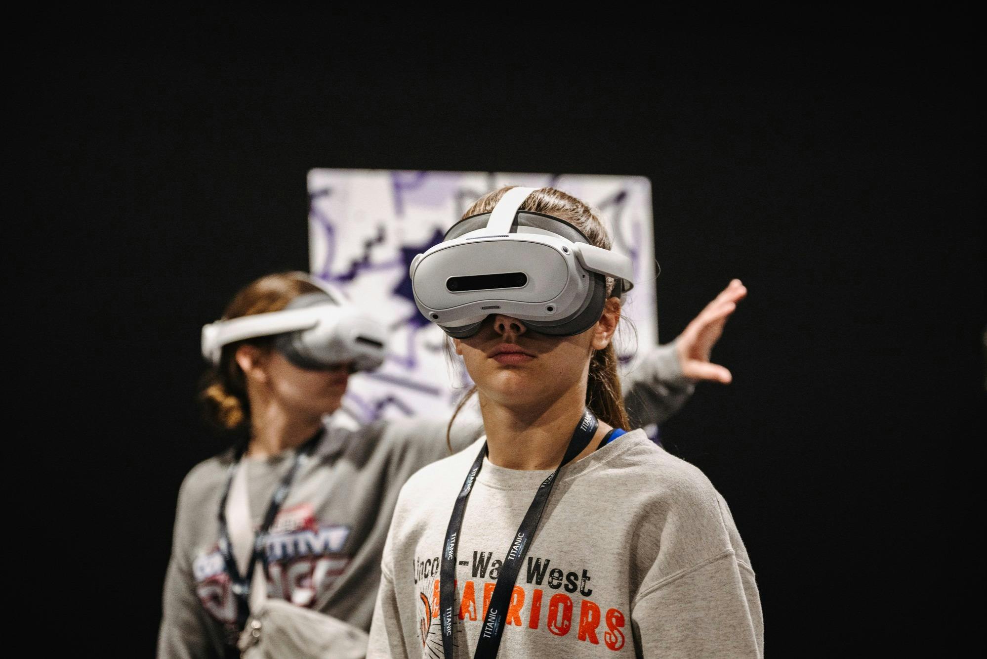 Two individuals wearing VR headsets in a dimly lit environment, one in the foreground and one slightly blurred in the background.