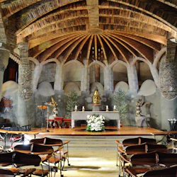 En utsmyckad kapellinteriör med välvda tegeltak, träbänkar, statyer, blomsterarrangemang och ett centralt altare.