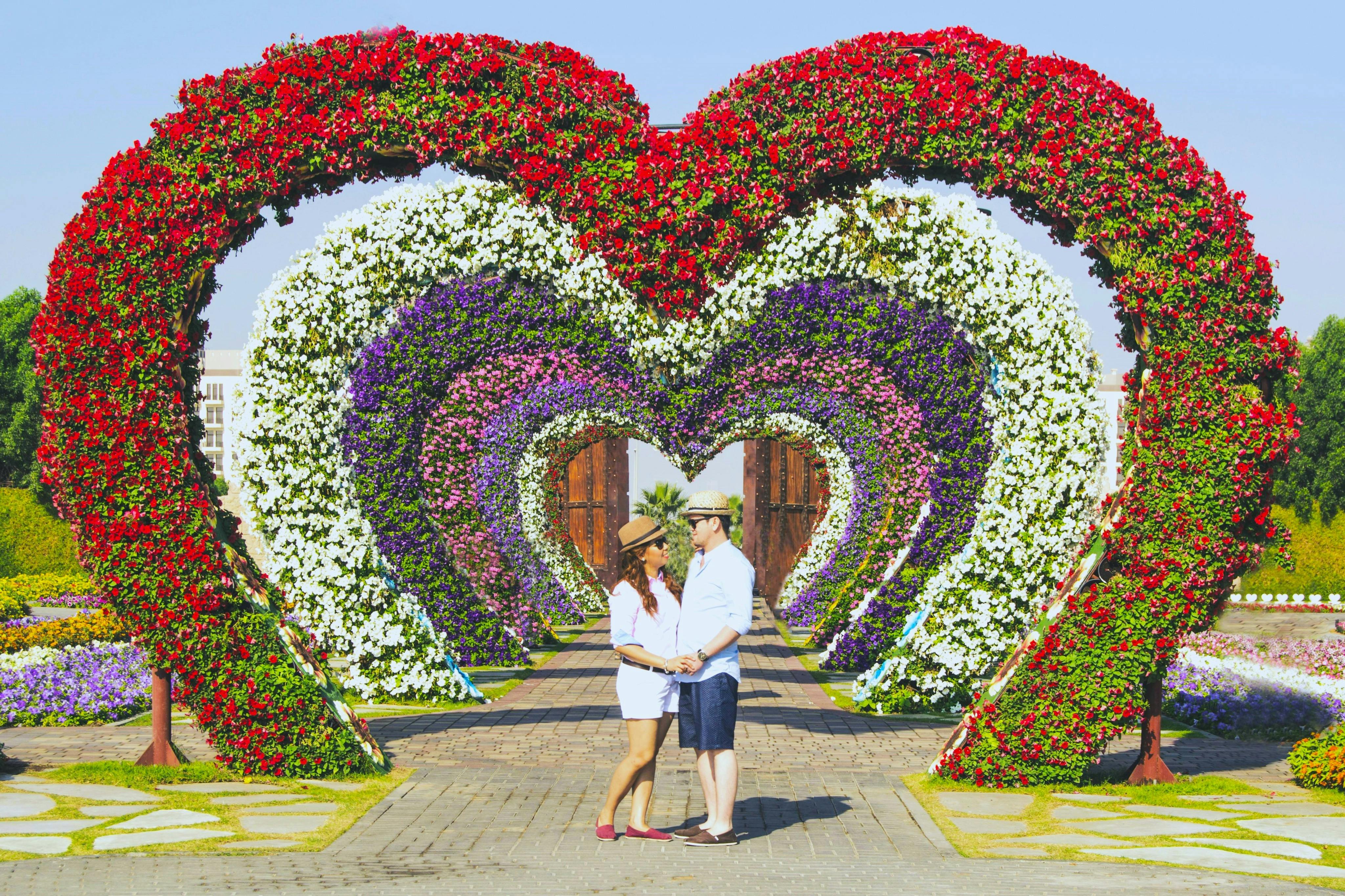 Una coppia si tiene per mano sotto grandi archi floreali a forma di cuore in un giardino.
