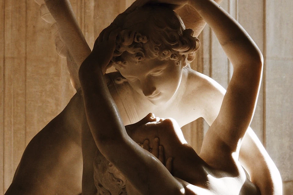 Close-up of a marble sculpture depicting two intertwined figures, one gently holding the other's head, with expressions of tenderness.