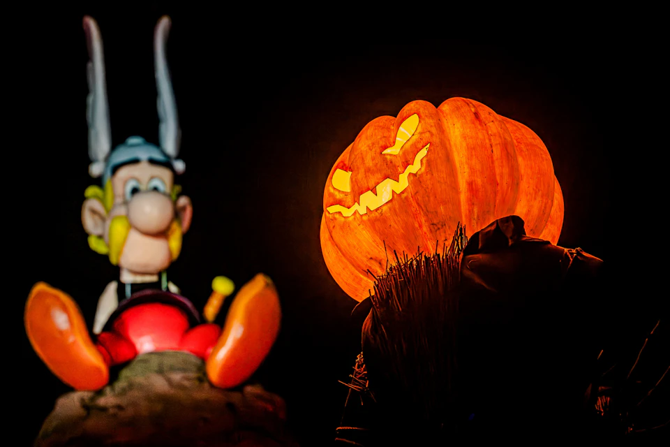 A glowing jack-o'-lantern with a mischievous face and a cartoon figure in the background, against a dark setting.