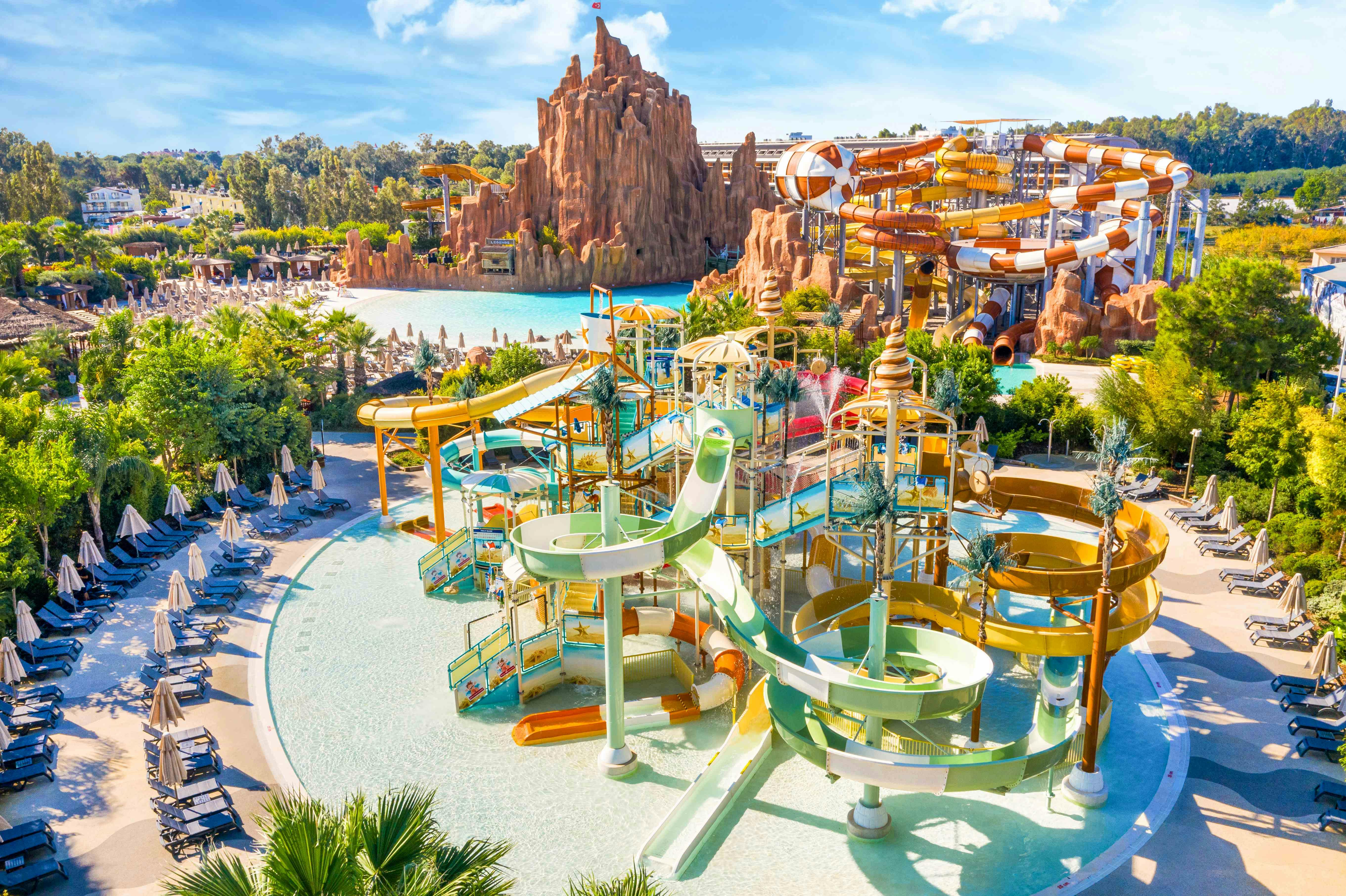 A vibrant water park featuring colorful slides, a pool, and decorative structures, set against a backdrop of rocky terrain.