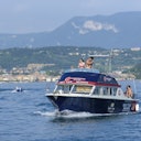 A boat with passengers on a lake, with mountains and a town visible in the background under a clear sky.