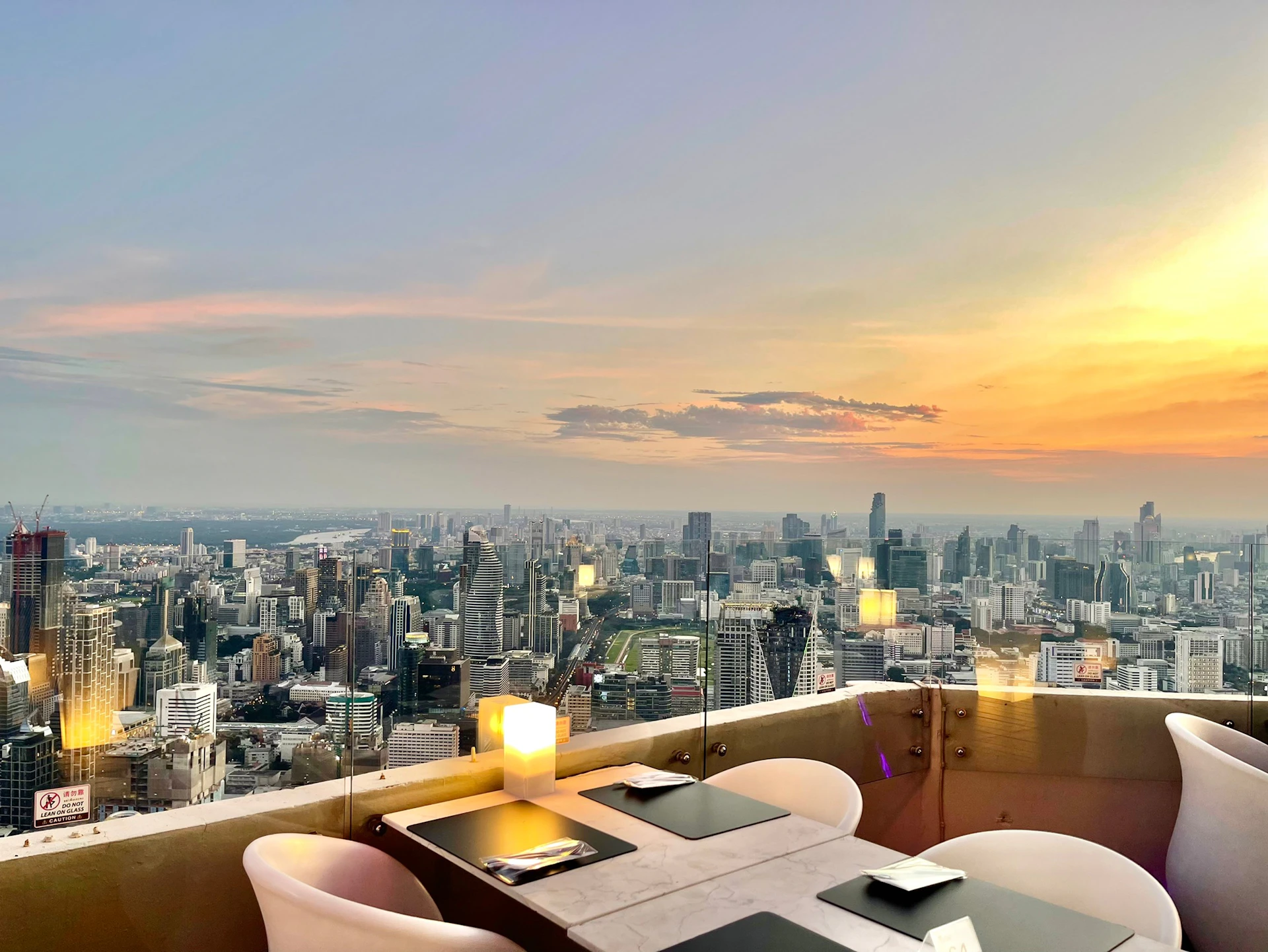 A rooftop dining setup with tables and chairs overlooking a cityscape during sunset.