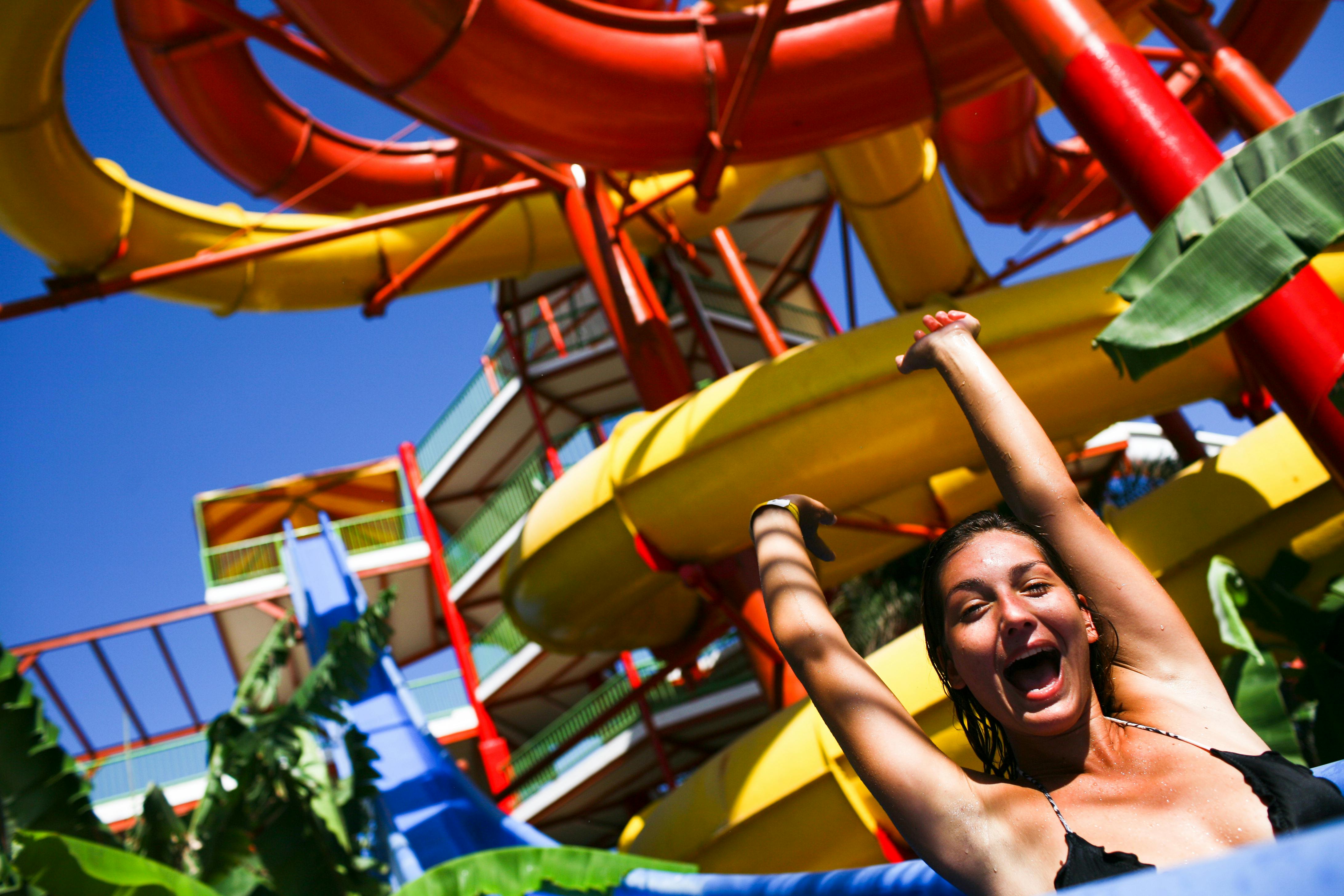 Smilende person på en vandrutsjebanetur, omgivet af farverige, loopende rutsjebaner og blå himmel i baggrunden.