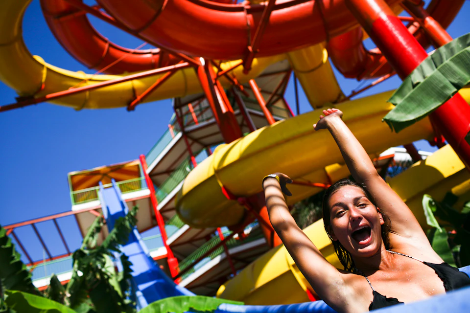 Smiling person on a water slide ride, surrounded by colorful, looping slides and blue sky in the background.