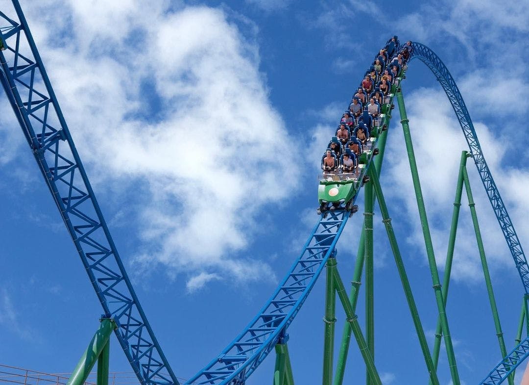 A roller coaster on a steep blue track against a blue sky with white clouds, filled with people enjoying the ride.