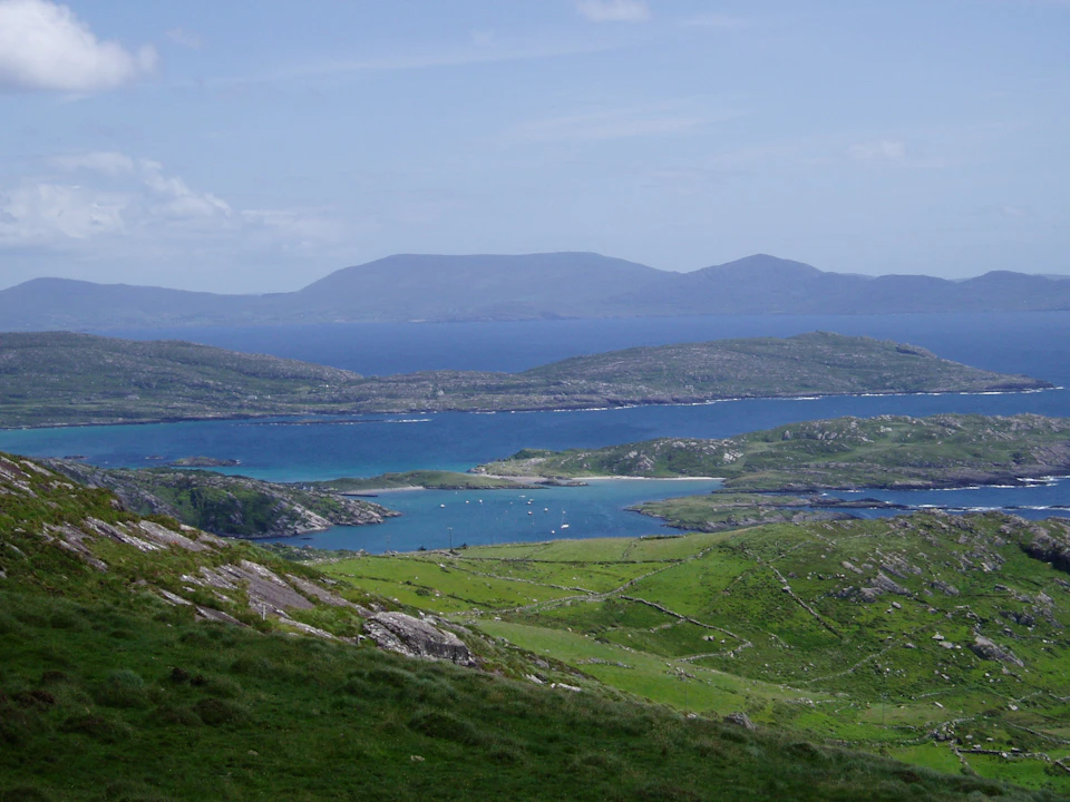 Overlooking a hilly green landscape with distant islands and a calm blue sea under a clear sky.