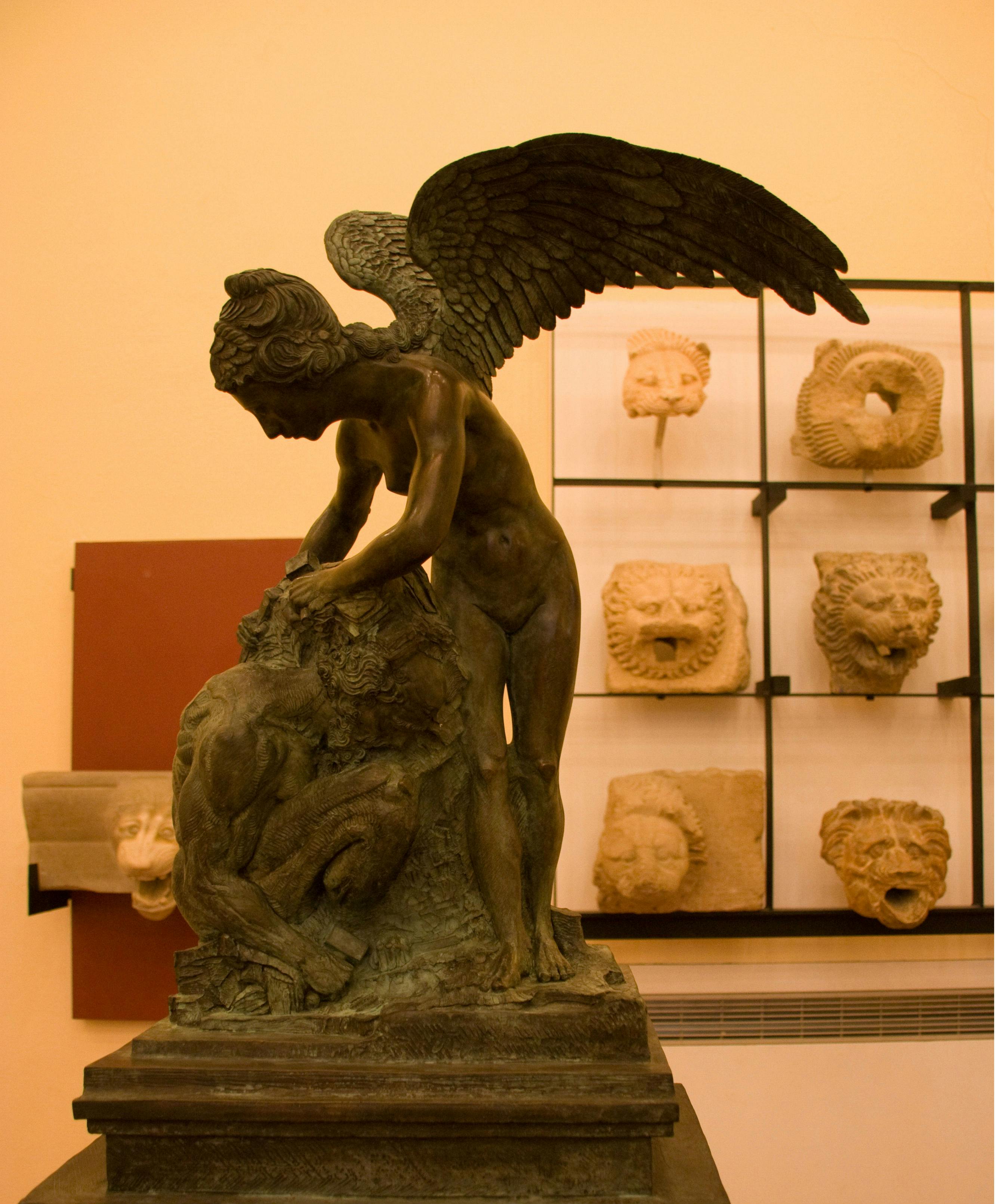 青铜雕像，翅膀形状，安慰坐着的男人，背景为壁挂式狮子头雕塑。