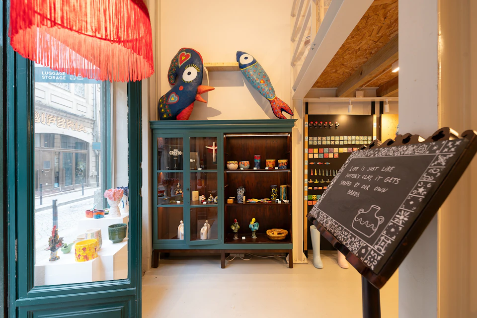 A cozy storefront with a teal cabinet displaying various items, colourful fish pillows on top, and decor on a chalkboard stand.