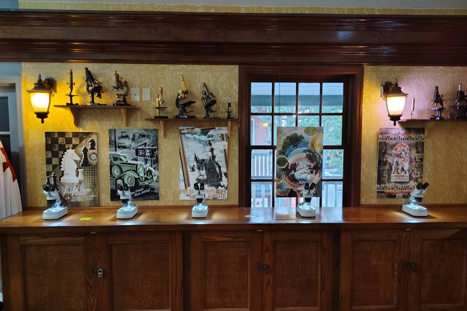 A wooden cabinet with microscopes on top and vintage posters on the wall, near a window showing an outdoor view.