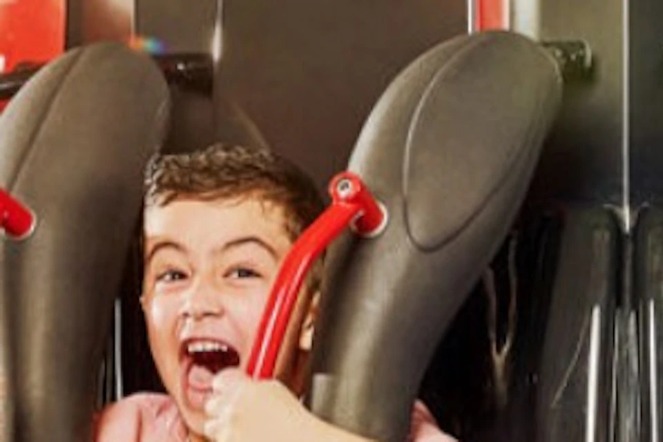 People seated on an amusement park ride, smiling and enjoying the experience, with a bright indoor setting in the background.