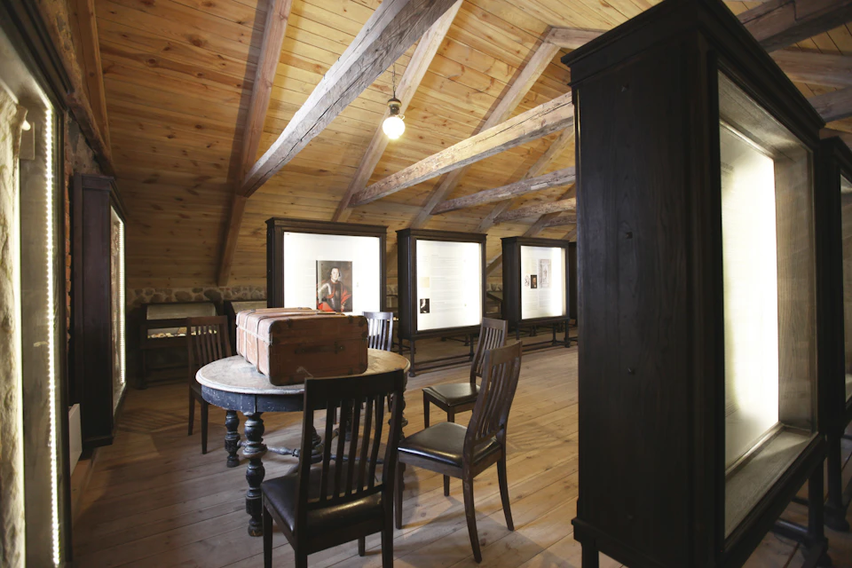 Wooden interior with a round table and chairs, showcasing framed pictures and text on easels against the walls.
