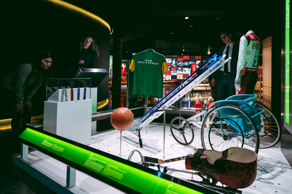 Exhibit displaying sports equipment, a "Team South Africa" jersey, a basketball, and a wheelchair in a museum setting.