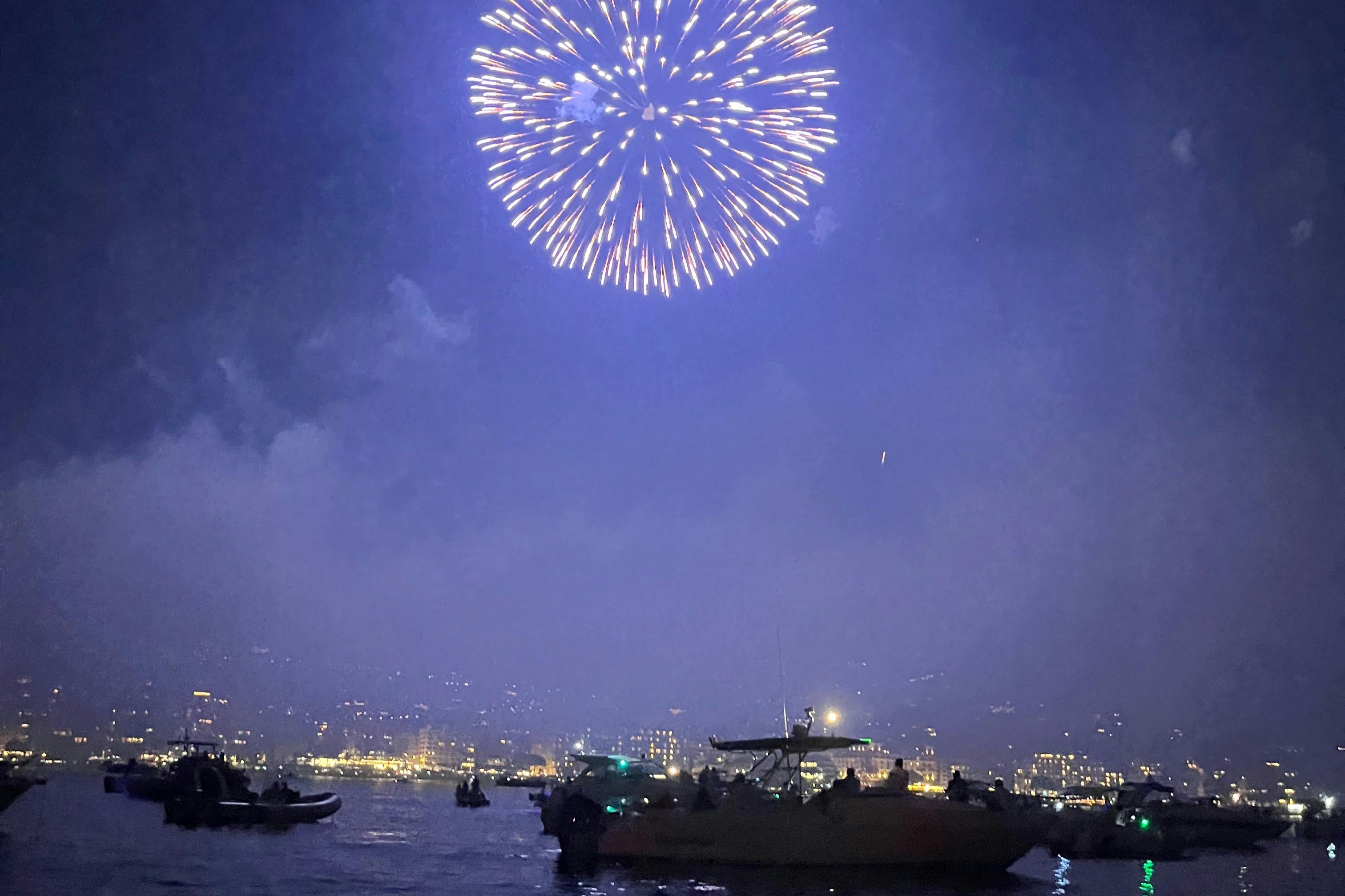 Fireworks light up the night sky over a cityscape and boats on water.