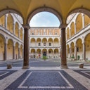 Interior courtyard of a historic building, featuring arched walkways, columns, and a central open space with a tiled ground.
