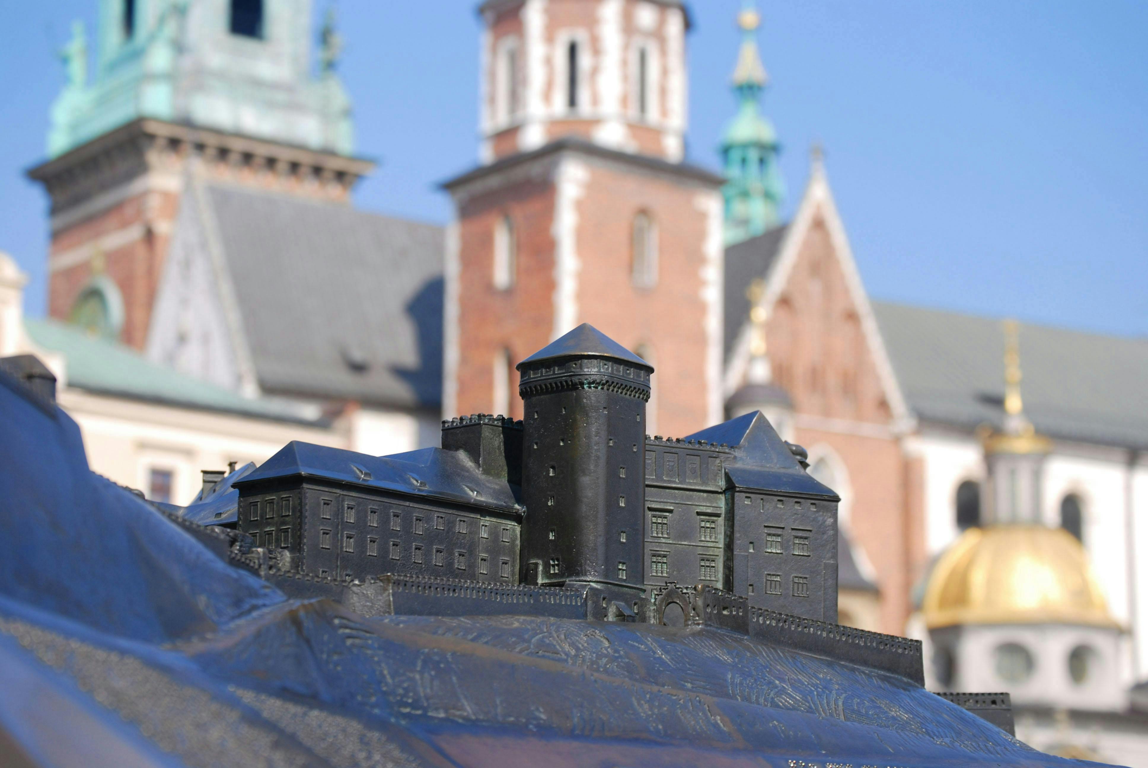 Detailed close-up of a miniature castle model with blurred historic brick buildings in the background.