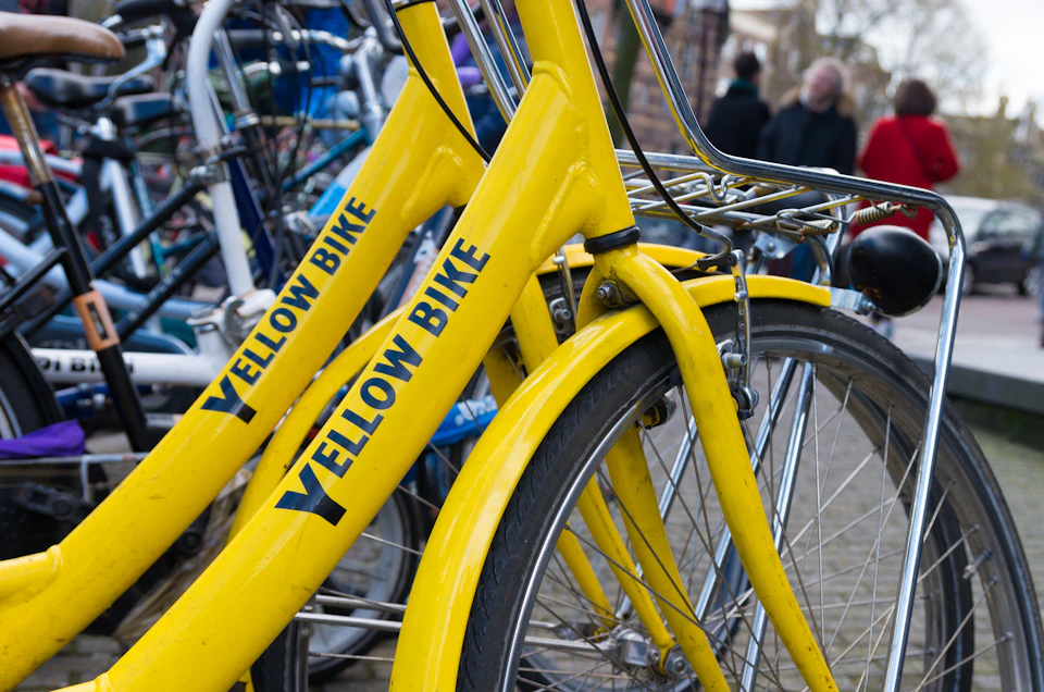 Cluster of yellow bicycles labeled "Yellow Bike" parked near other bikes. Some people are blurred in the background.