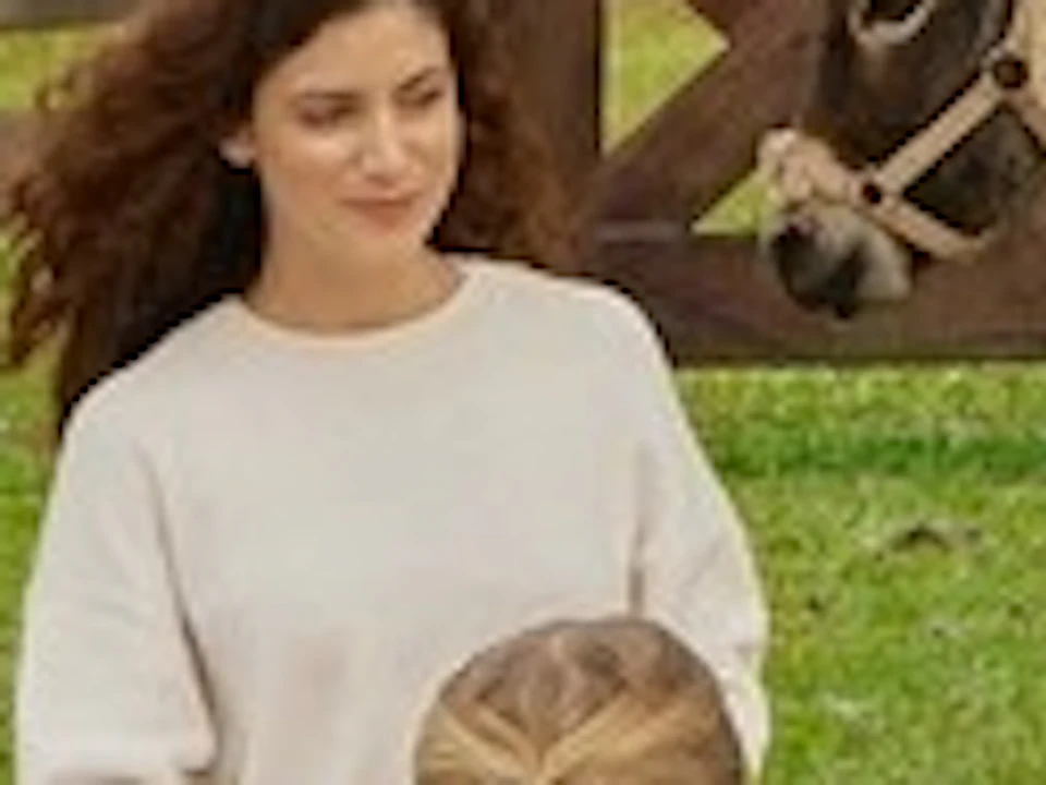 A family having a picnic on a mat outdoors, surrounded by greenery and three donkeys near a tree.