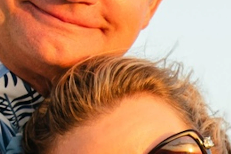 A couple smiling on a boat, with ocean water and a blue sky in the background.