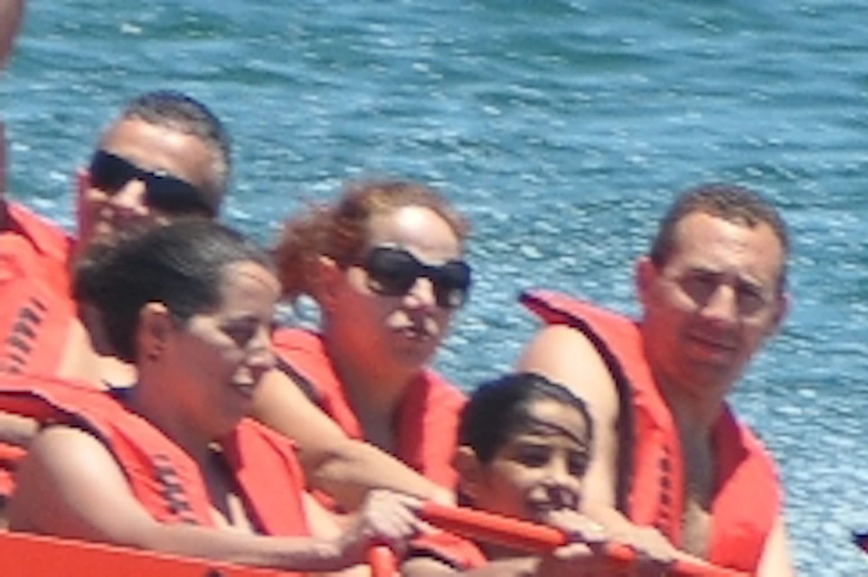People enjoying a ride on an orange jet boat with a black-and-white checkered design, speeding across the water.