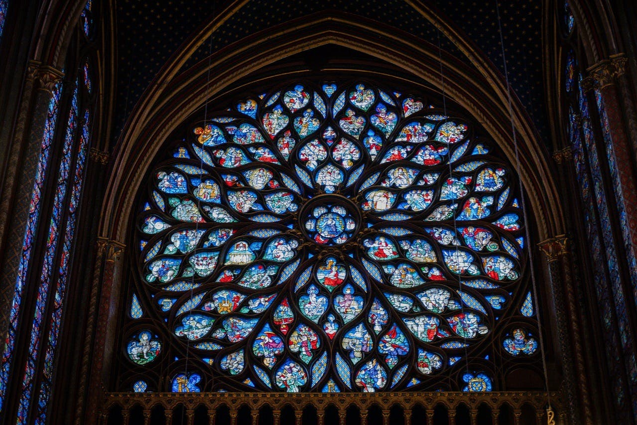 Intricate stained glass rose window with vibrant, detailed patterns in a darkened Gothic cathedral.