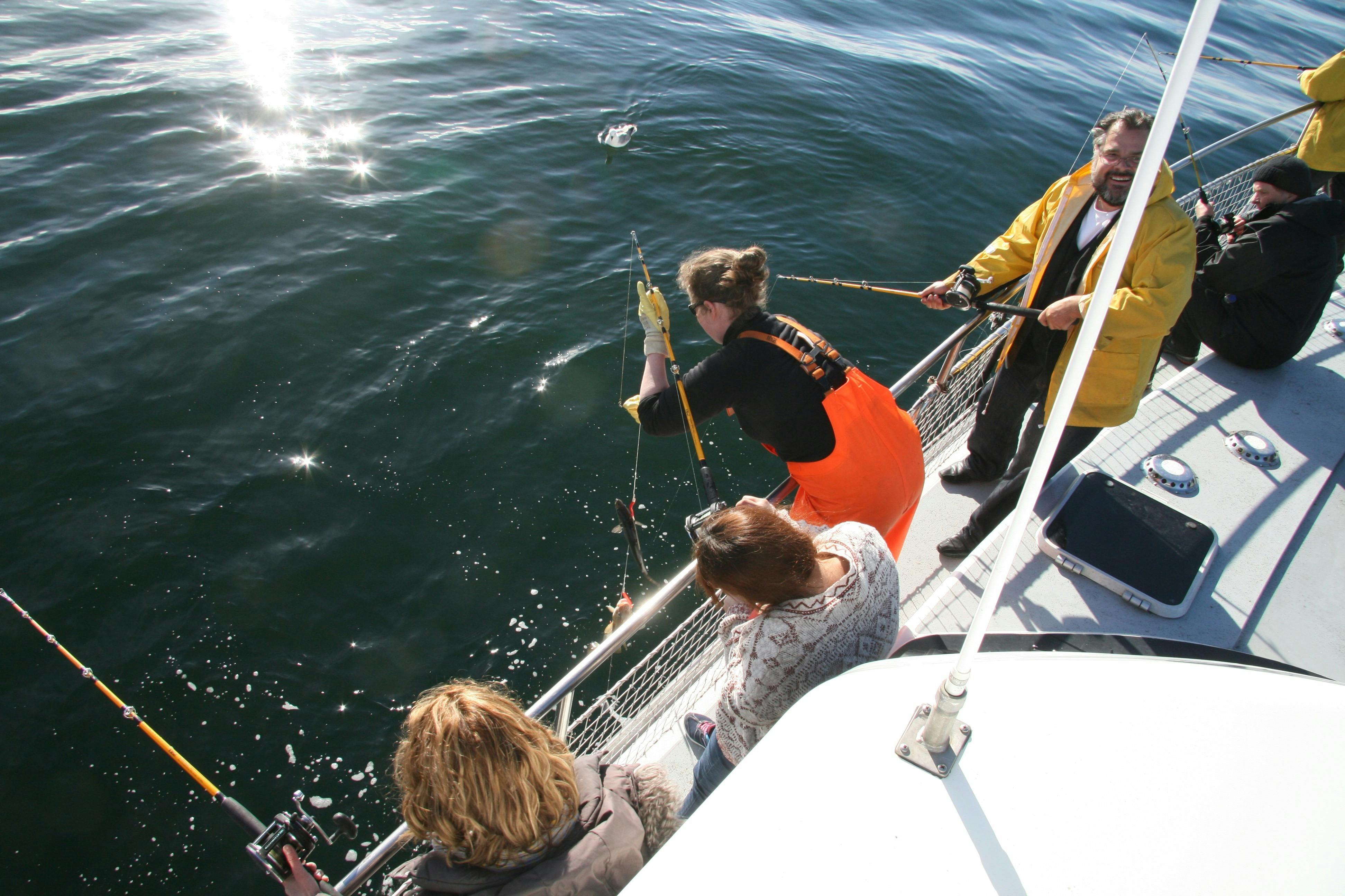 En fisker har fanget en fisk, og guiden hjælper med at rulle den ind i båden.