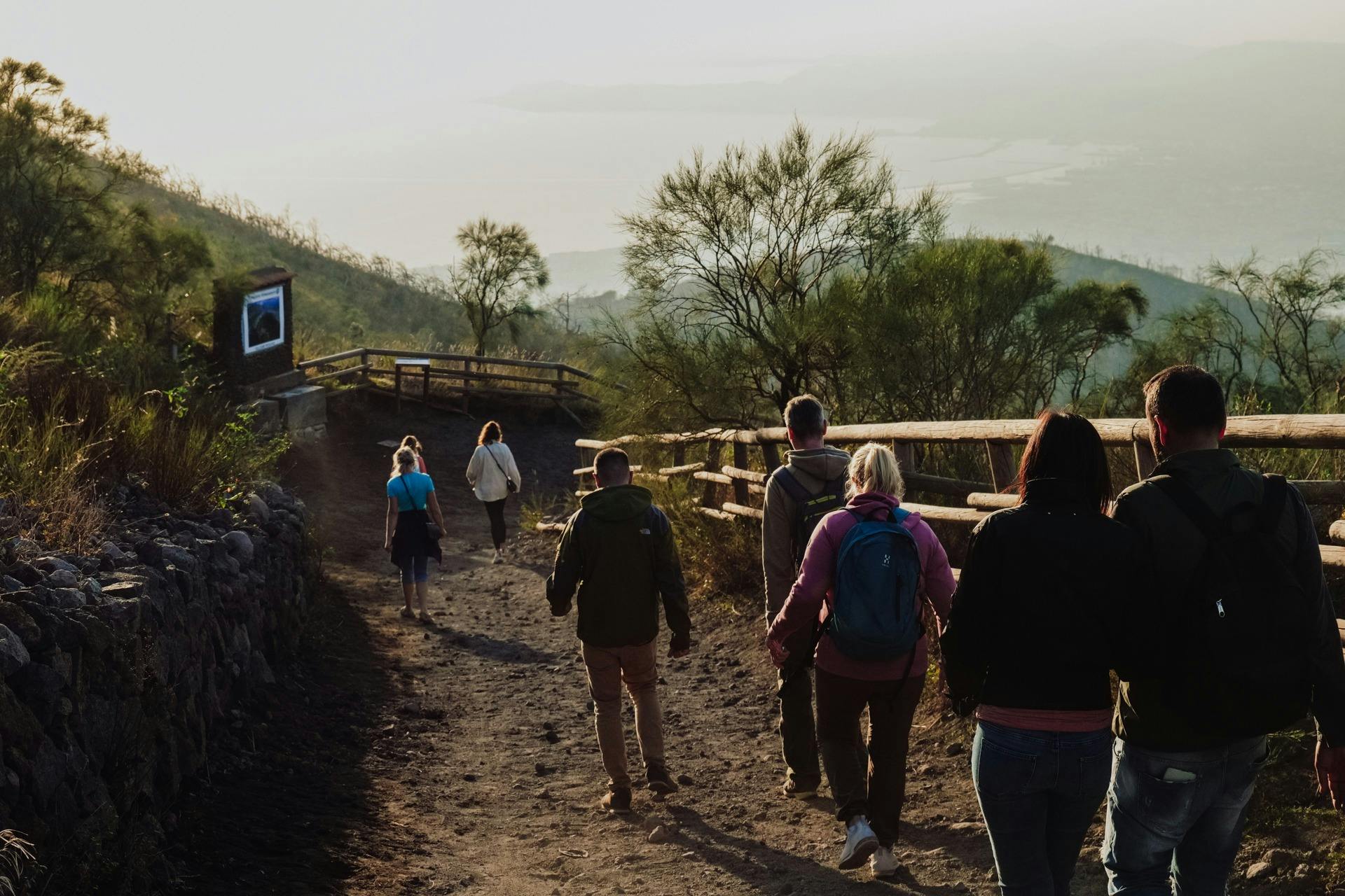 Un groupe de personnes marchant sur un chemin de terre à flanc de colline, bordé de clôtures en bois et d'arbres clairsemés.