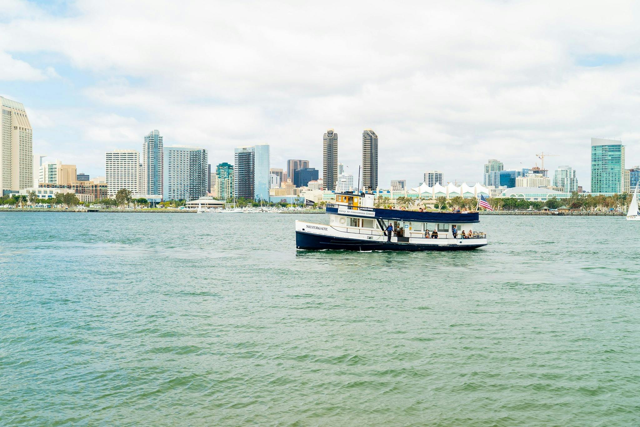 前景中有一艘小客船，拥有城市天际线，背景是多云的天空下的高楼大厦。