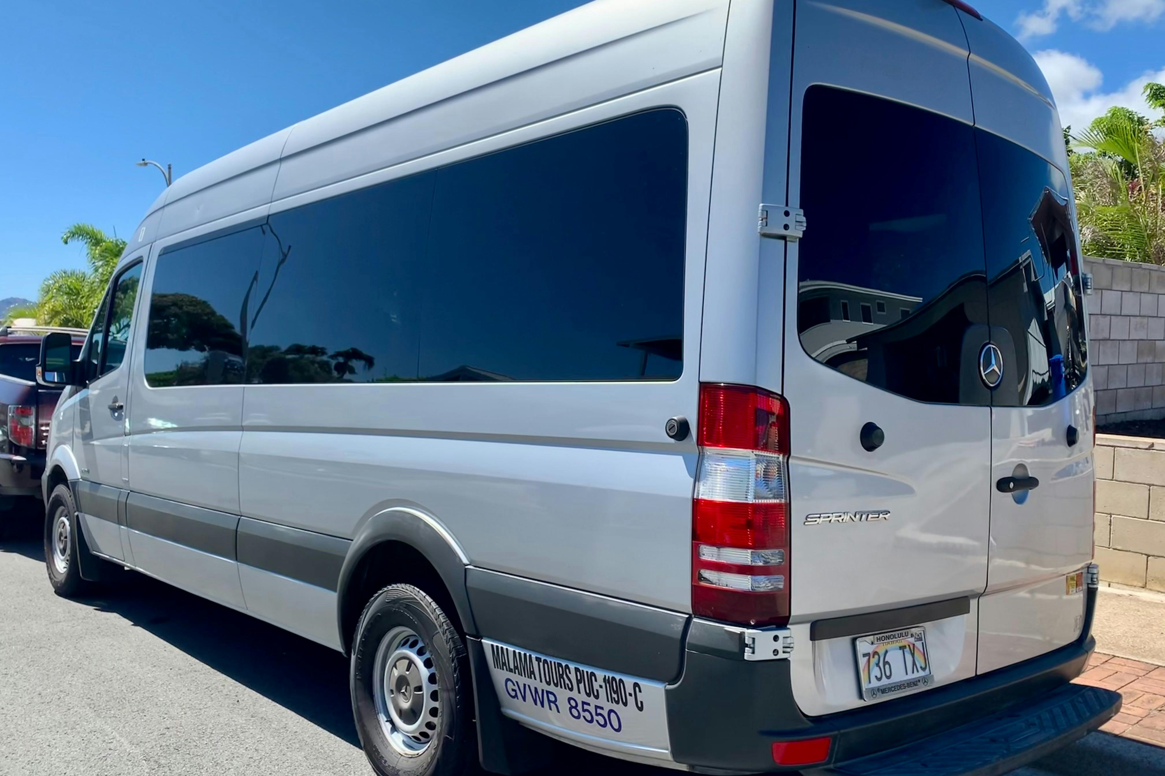 A grey tour van with "Malama Tours" sign and license plate parked on a sunny street.