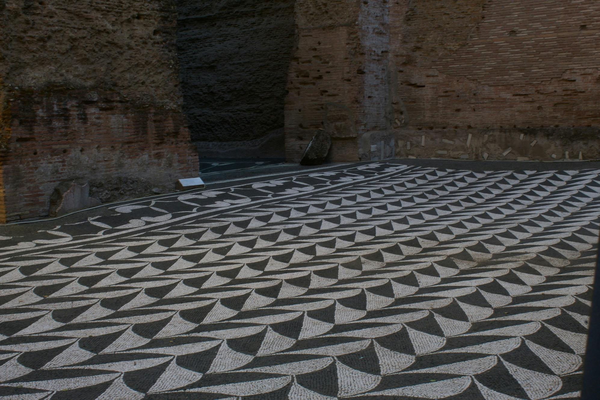 黒と白の幾何学的なモザイクの床のパターンは、粗い茶色のレンガの壁と地面の小さな看板の隣にあります。