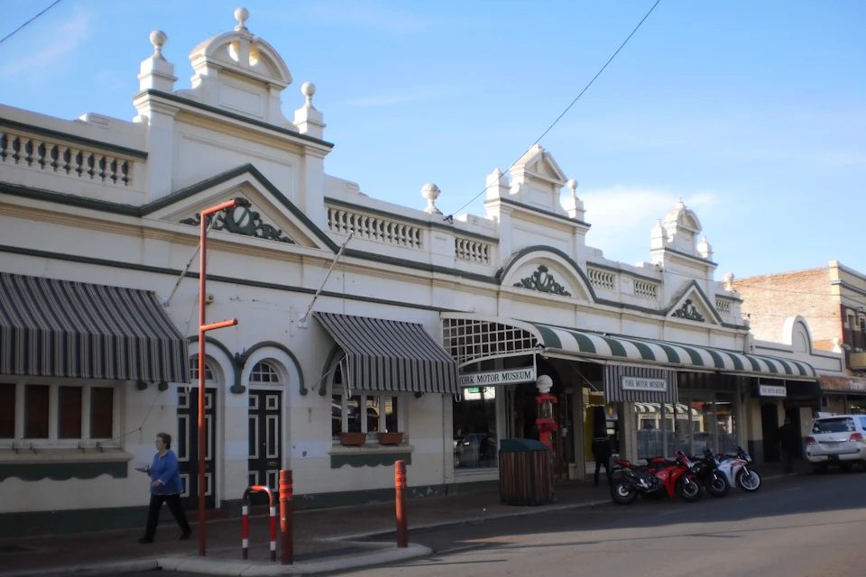 A historic building with decorative arches, striped awnings, and a sign reading "Motor Museum." Motorcycles are parked outside.