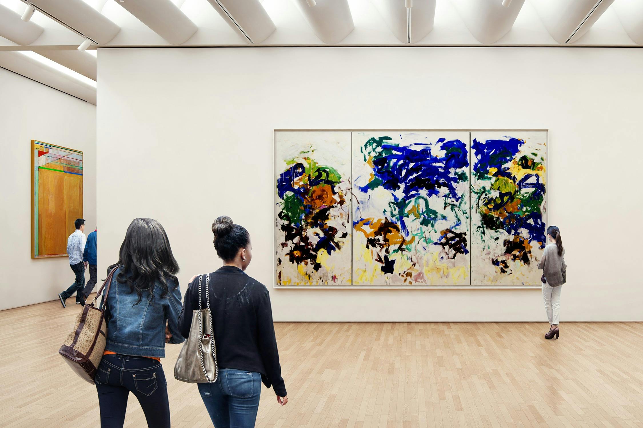 Two people viewing a large abstract triptych painting in a bright art gallery with a wooden floor.