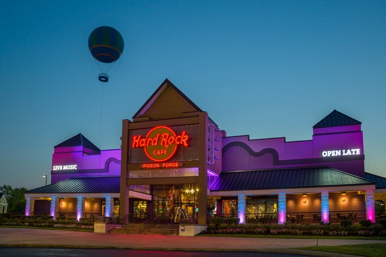 Exterior of Hard Rock Cafe Pigeon Forge at dusk, with neon signage and a hot air balloon in the sky.
