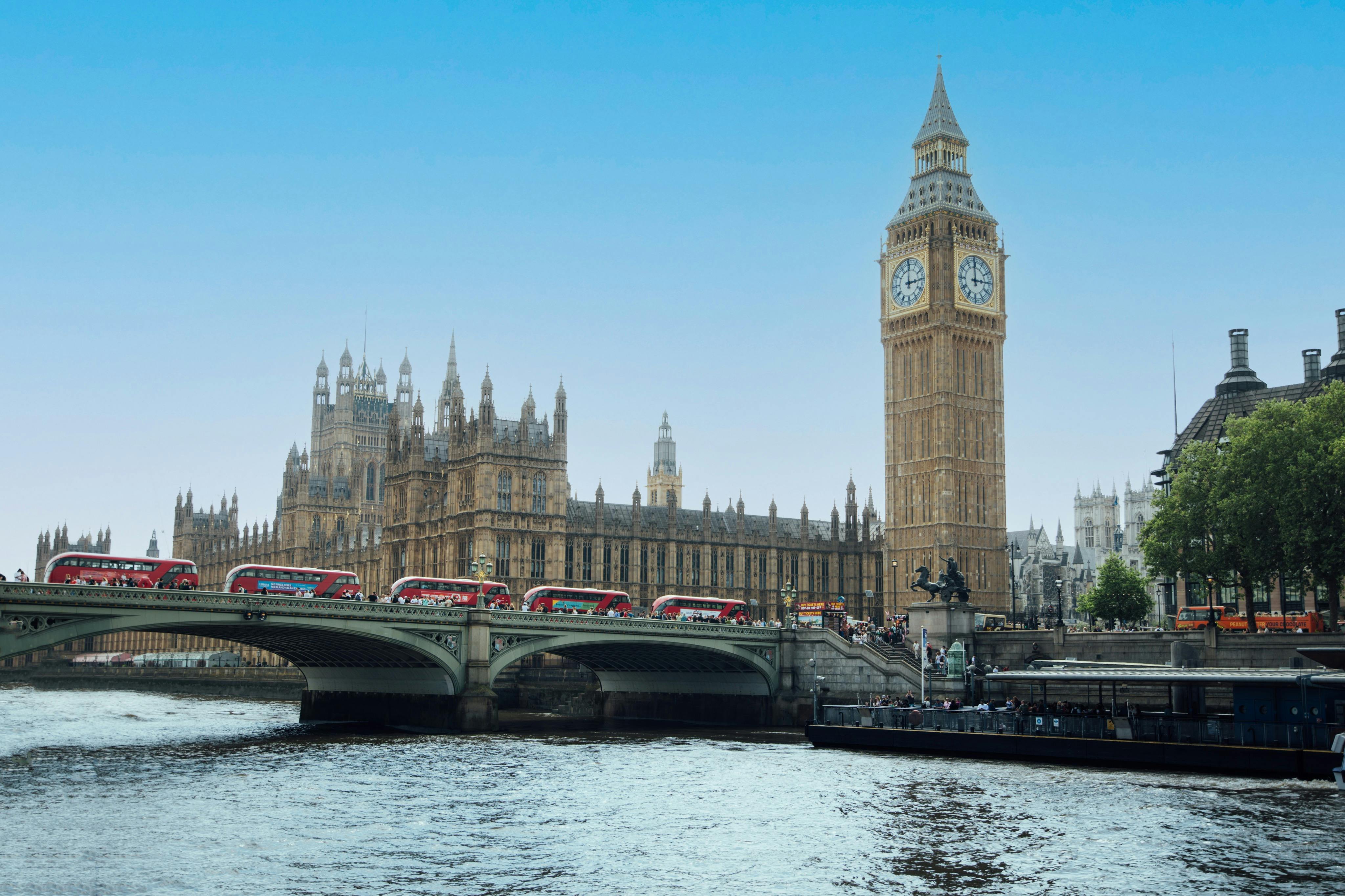 Vue du palais de Westminster et de Big Ben près de la Tamise, avec des bus rouges à impériale traversant un pont.