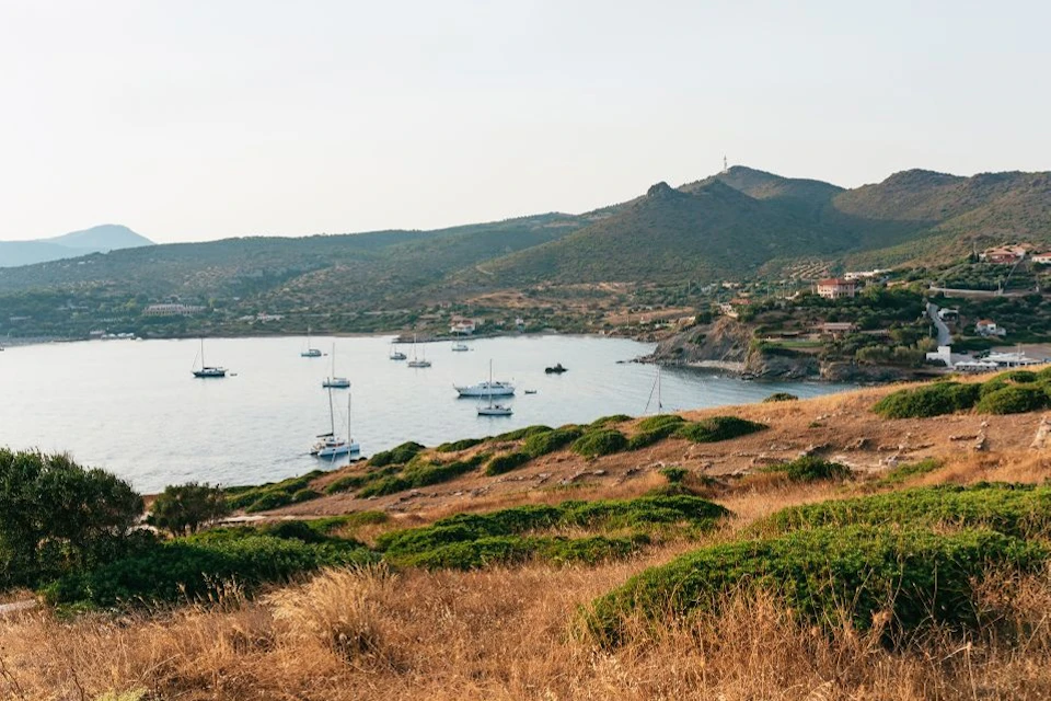 Yachts anchored in a calm bay surrounded by dry, grassy hills and small hills in the background under a clear sky.