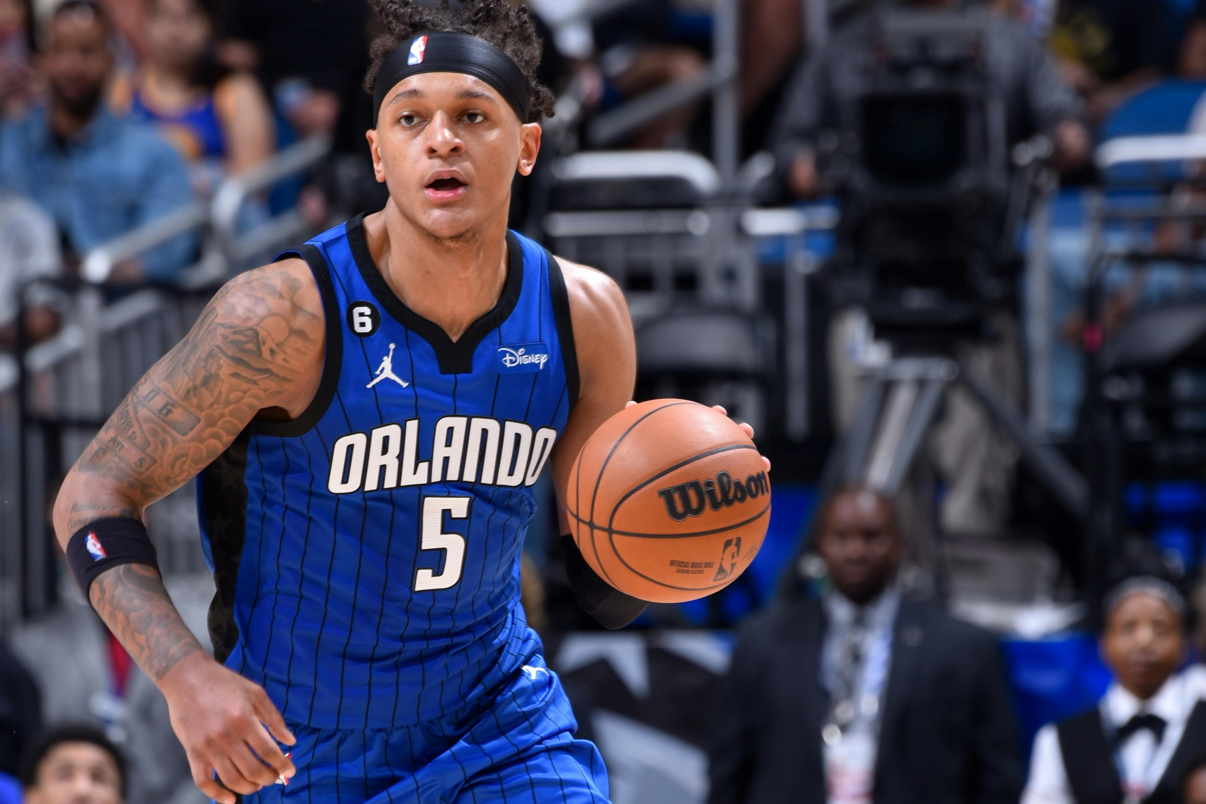 Μπασκετμπολίστας με μπλε φανέλα του Ορλάντο που κρατά μια μπάλα του μπάσκετ, στα μέσα της δράσης στο γήπεδο.