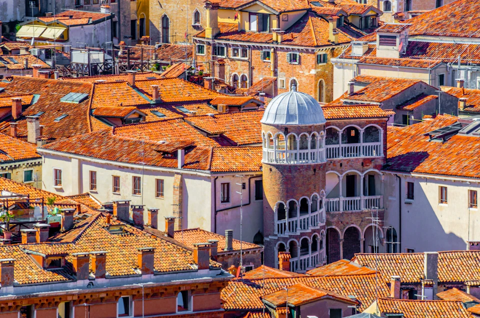 Aerial view of a cluster of traditional buildings with vibrant red-tiled roofs and a rounded tower featuring arched windows.