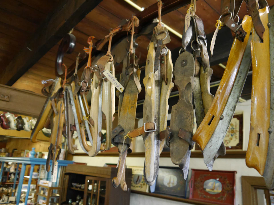 Vintage ice skates hang on wooden beams inside a rustic room filled with antique furniture and decorative items.
