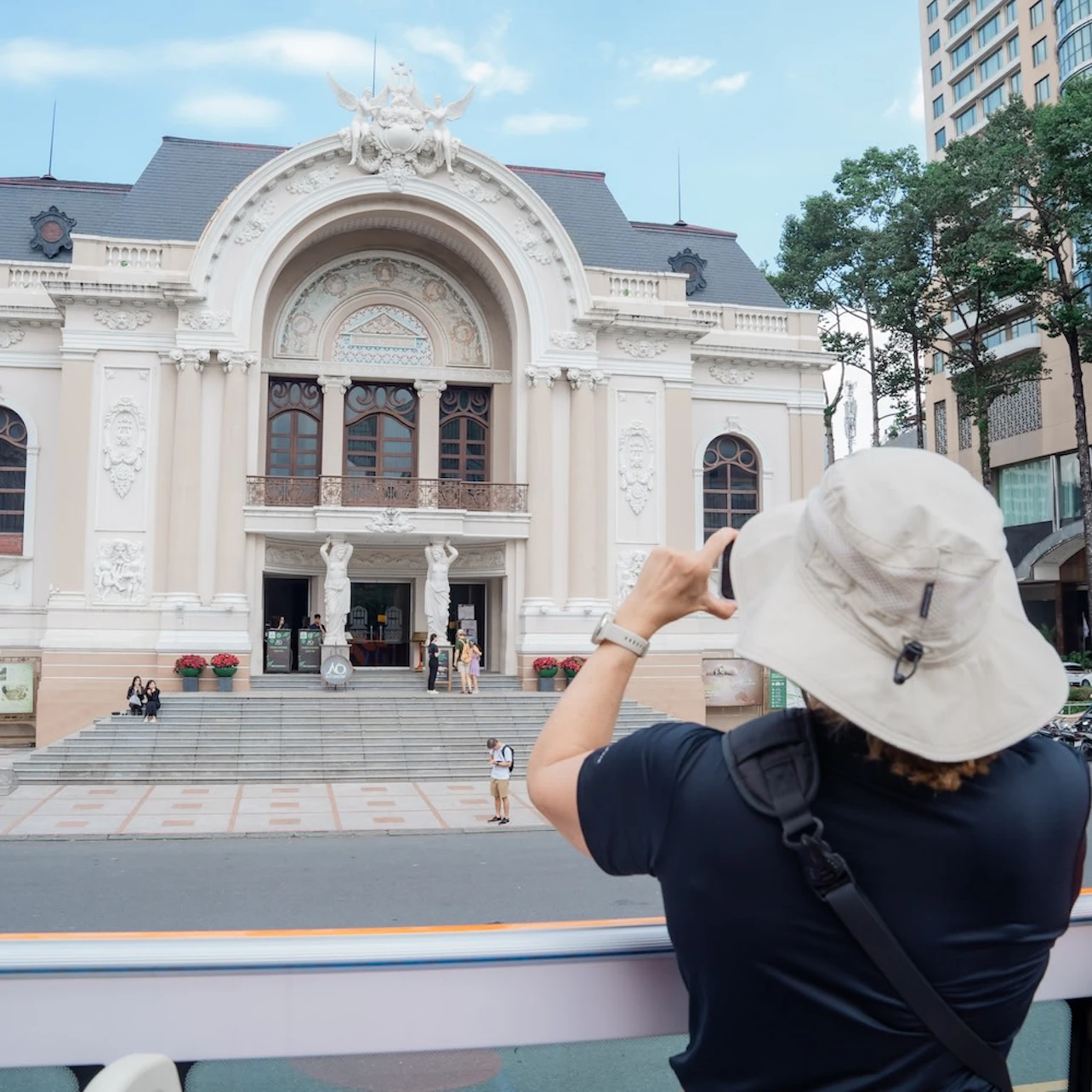 A person wearing a hat takes a photo of a grand building with ornate architecture and arched windows.