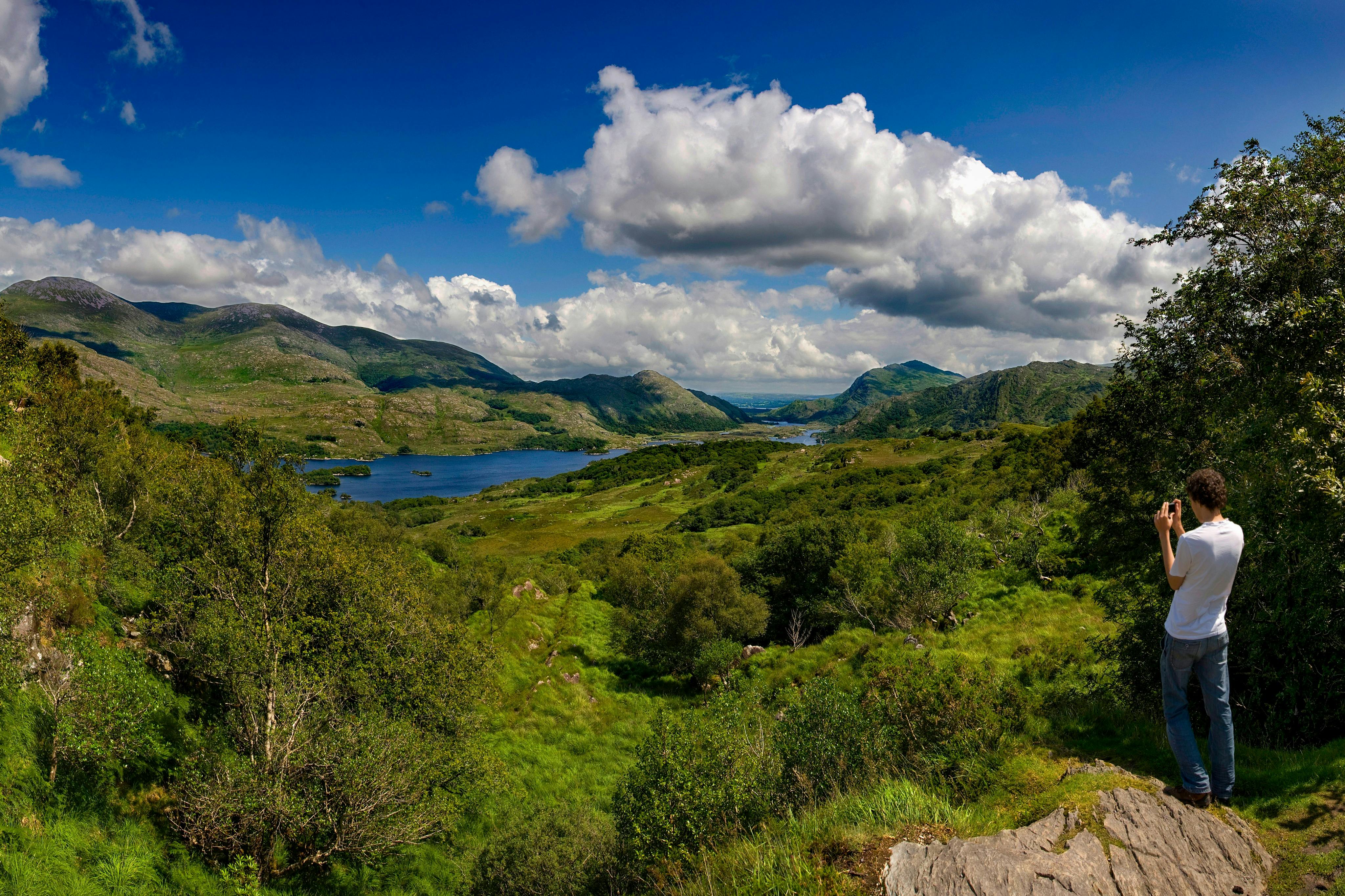 Scenic view of a lush green valley with a lake, surrounded by hills under a partly cloudy blue sky.