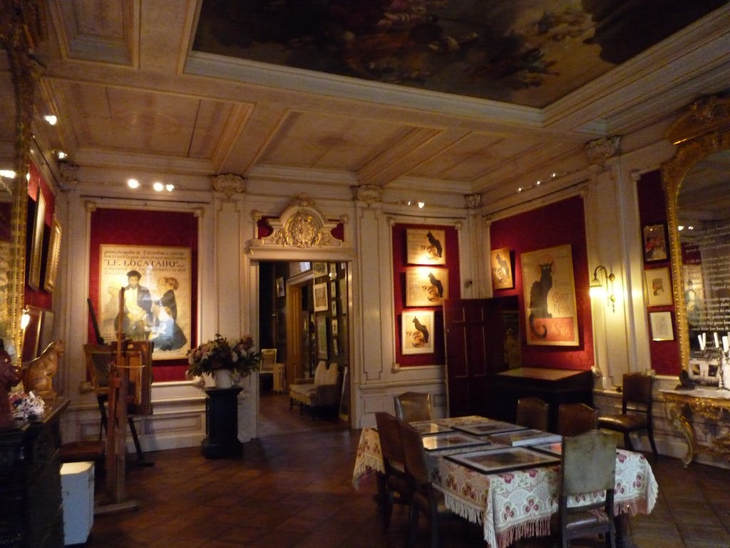 装饰华丽的房间，配有复古海报、带框的猫咪插图、木制家具、装饰天花板和套装餐桌。