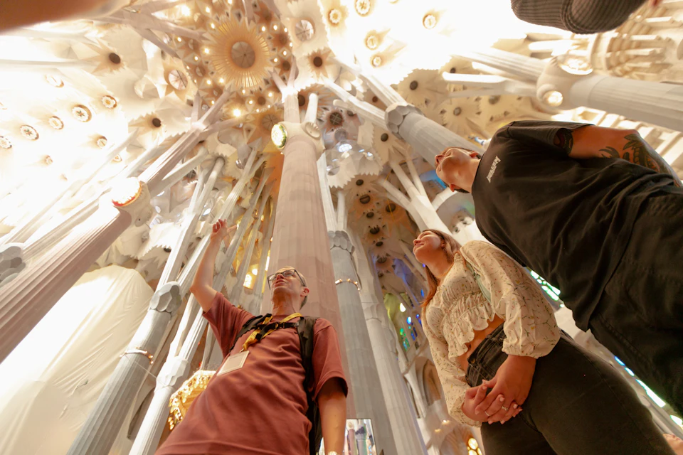 People standing inside a grand cathedral, looking up at the intricately designed ceiling and tall columns.